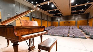 A grand piano and bench in a spacious auditorium with rows of seats. - YMCA Asia Youth Center (Tokyo)