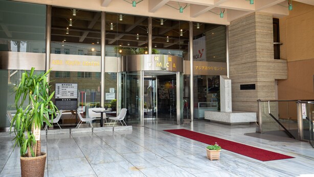 A modern building entrance with a glass door, indoor seating area, and a red carpet. - YMCA Asia Youth Center (Tokyo)