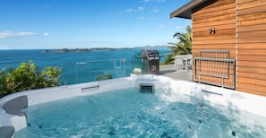 A hot tub with a clear view of the ocean and a wooden building in the background.