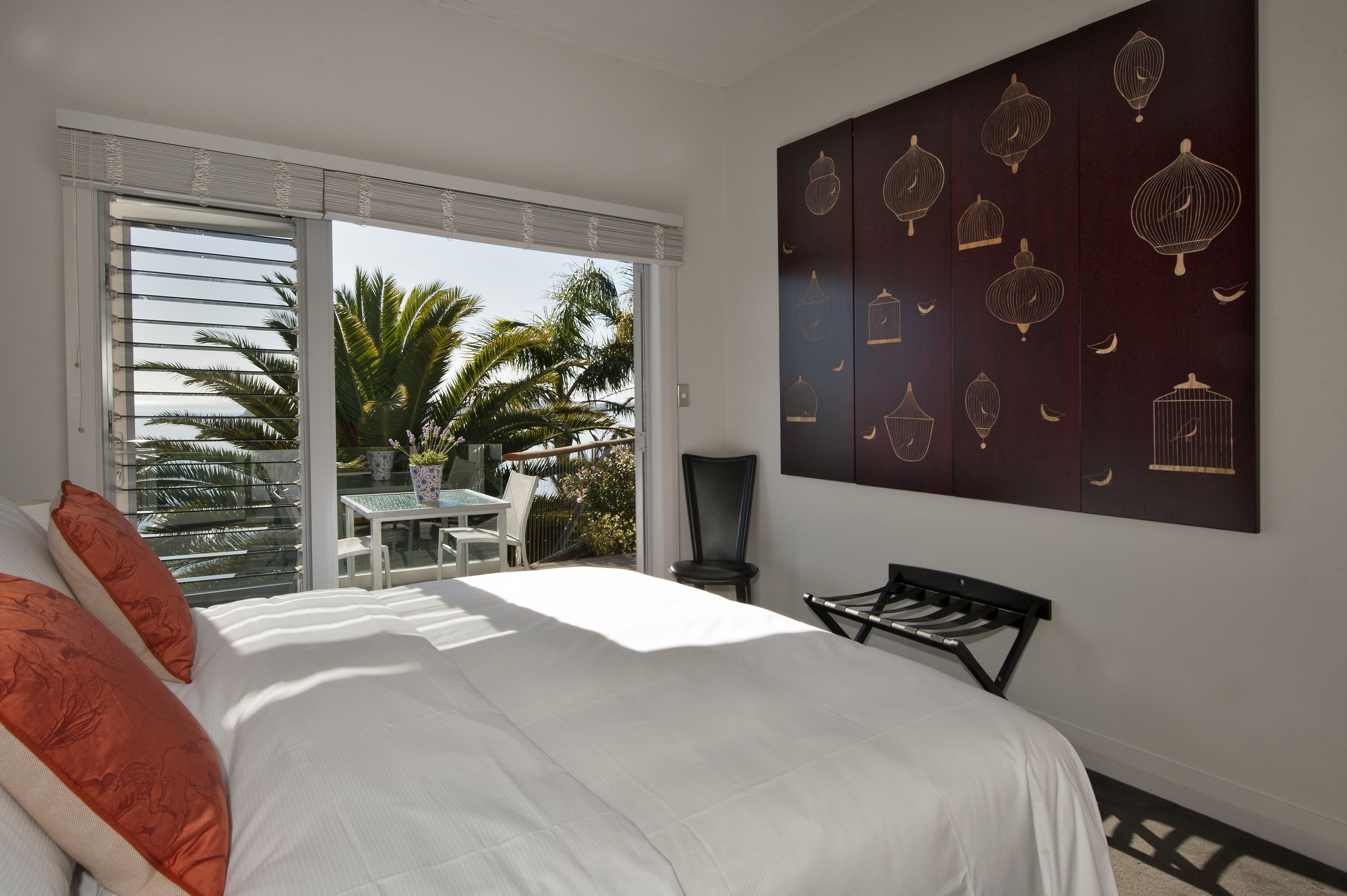 A bedroom with a bed, a table, chairs, and a balcony with palm trees.