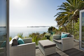 A balcony with wicker furniture, a glass railing, and a view of the sea. - Cloud 9 Luxury Villa (Russell)