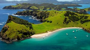 A coastal landscape with green hills, a sandy beach, and clear turquoise waters. - Cloud 9 Luxury Villa (Russell)