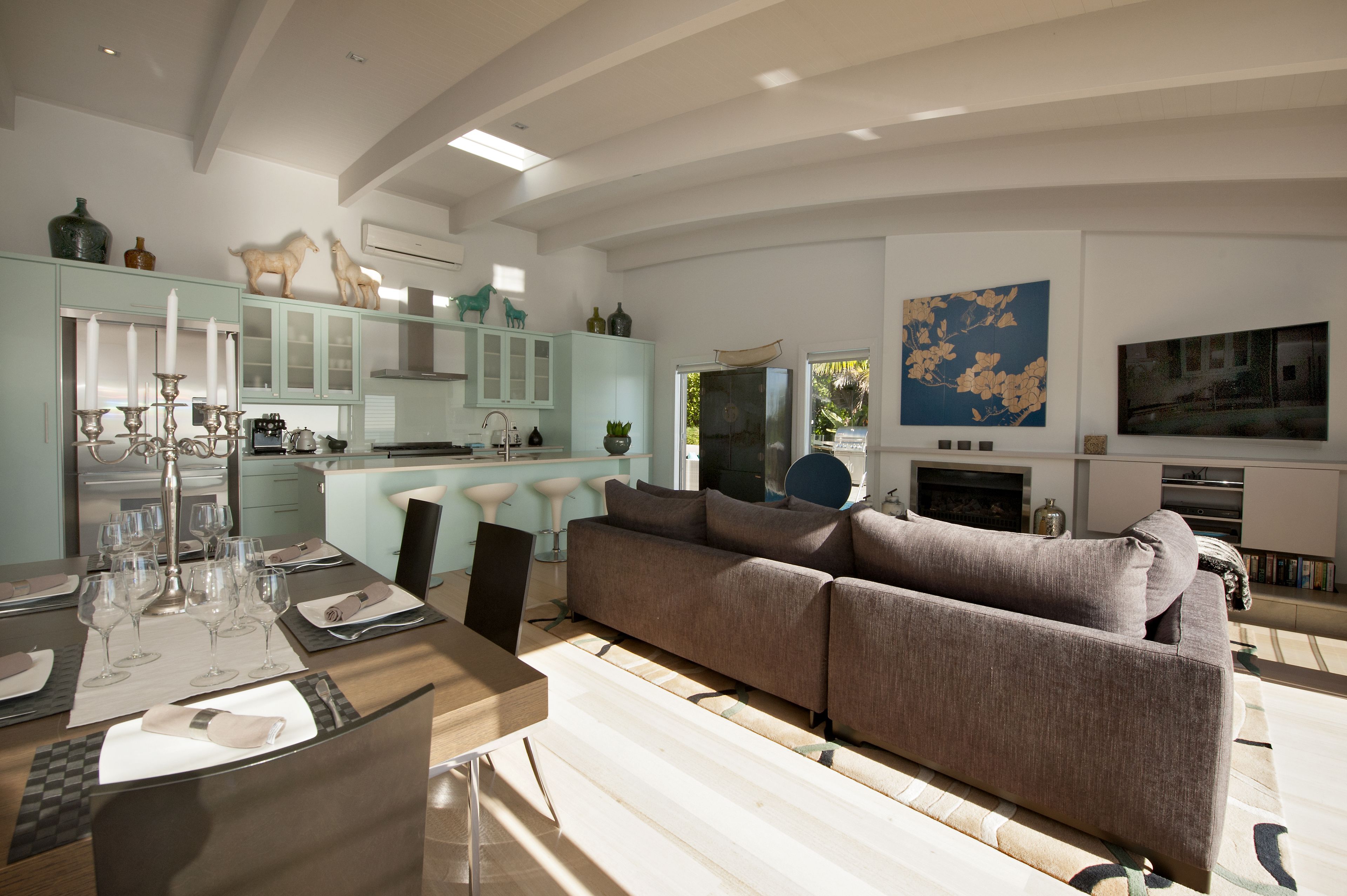 Een moderne woonkamer met een bank, een eettafel voor zes personen en een keuken met lichtblauwe kastjes en decoratieve objecten.