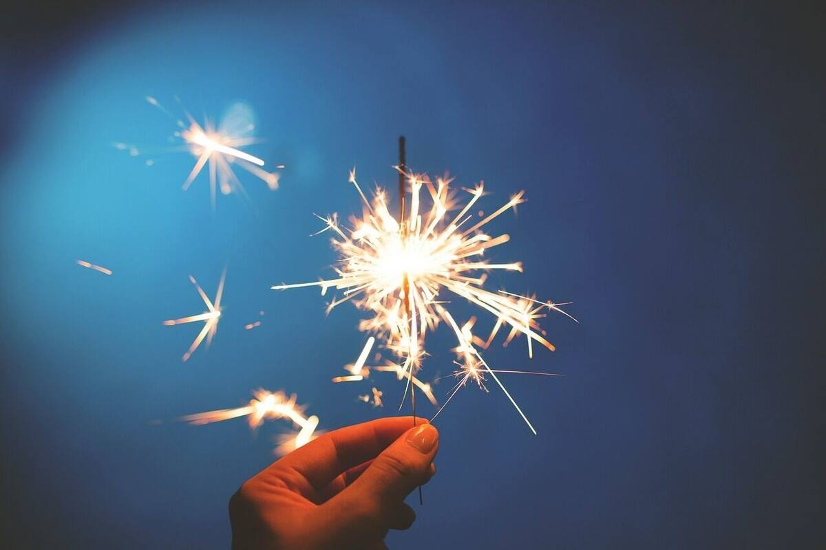 En hand håller i ett knallspjut, och gnistor sprider sig mot en mörkblå bakgrund.
