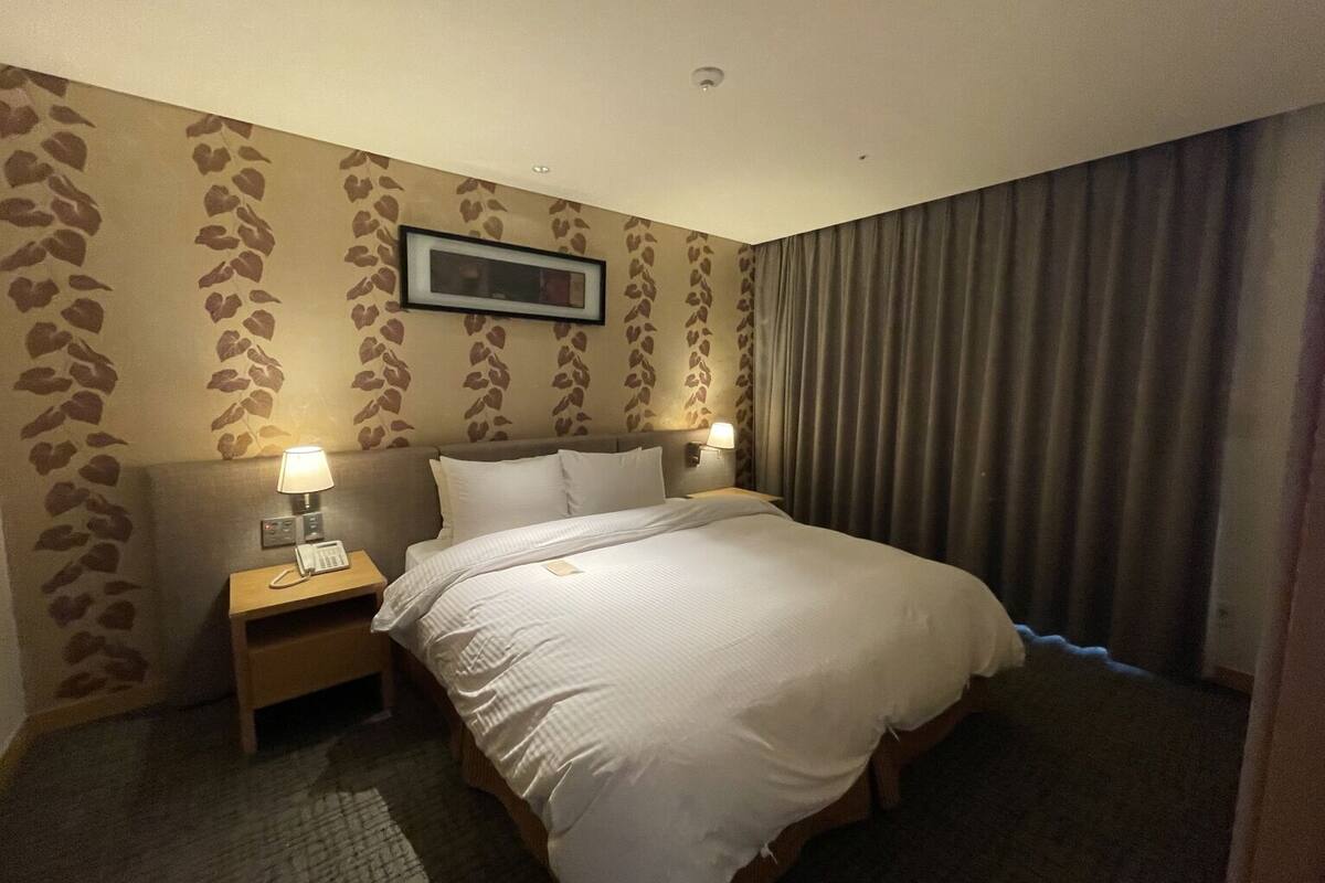 Ett hotellrum med en säng, två sängbord med lampor, en telefon och en inramad tavla på väggen.