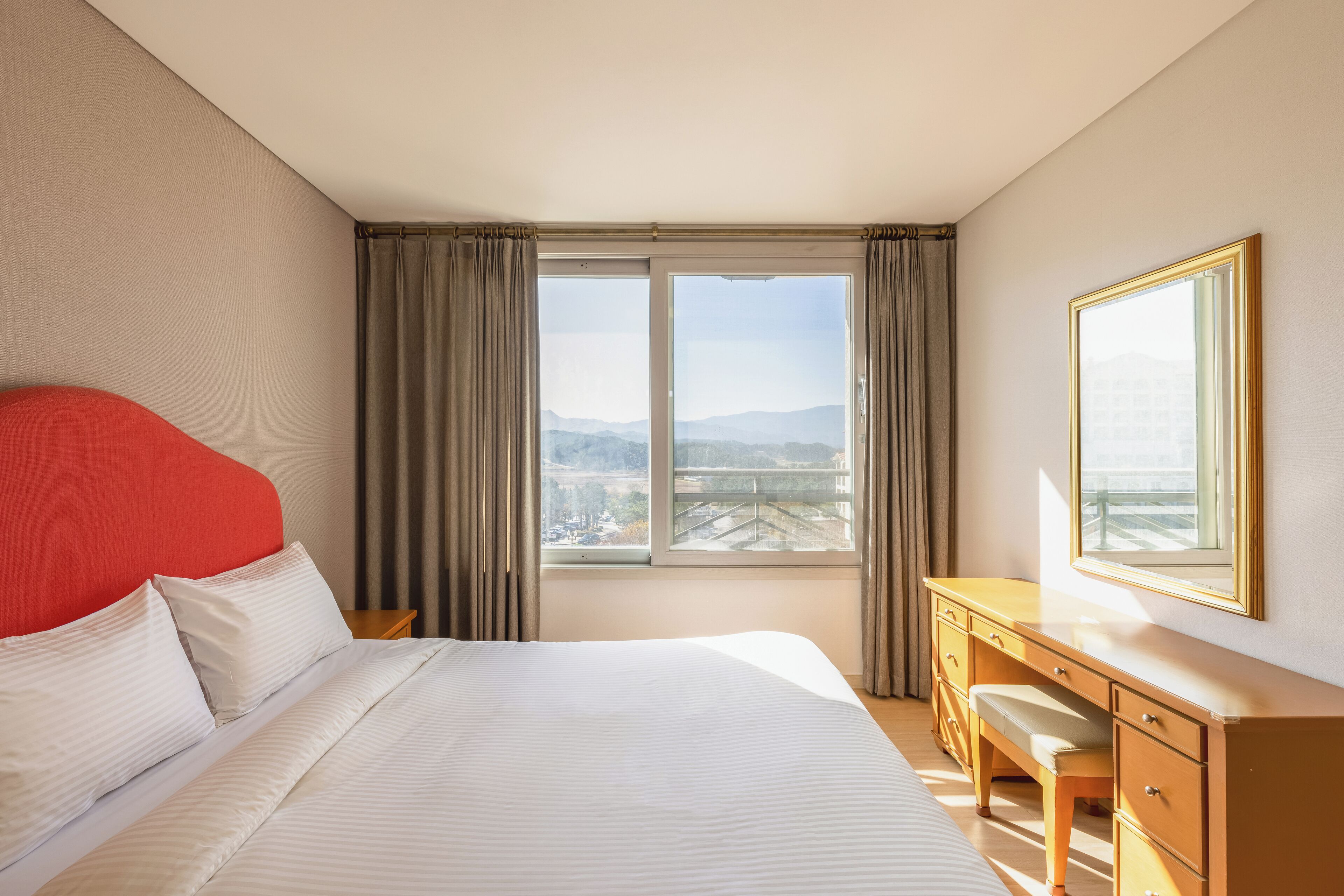 A hotel room with a large bed, a desk, and a view of a cityscape through the window.