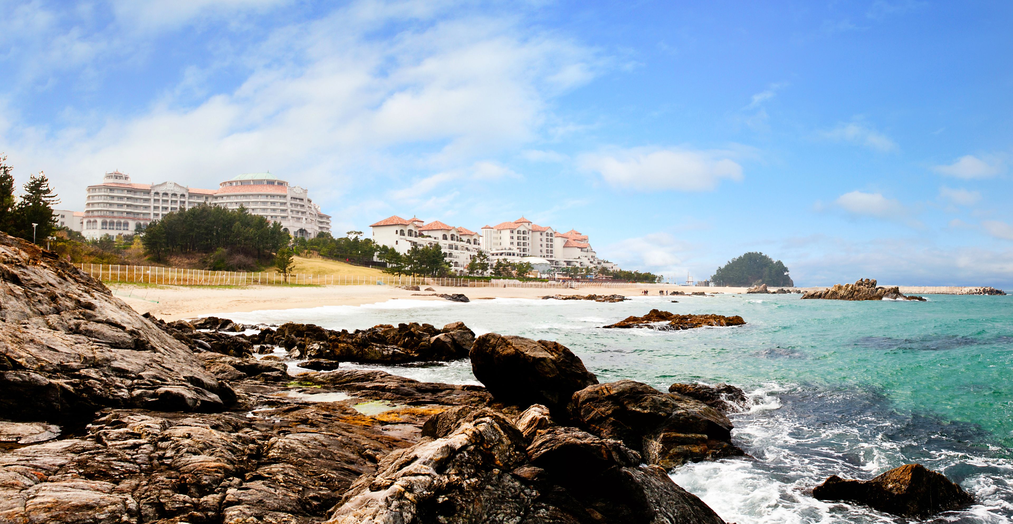 A coastal hotel with multiple buildings, a rocky shoreline, and clear blue waters.