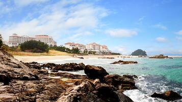 A coastal hotel with multiple buildings, a rocky shoreline, and clear blue waters.