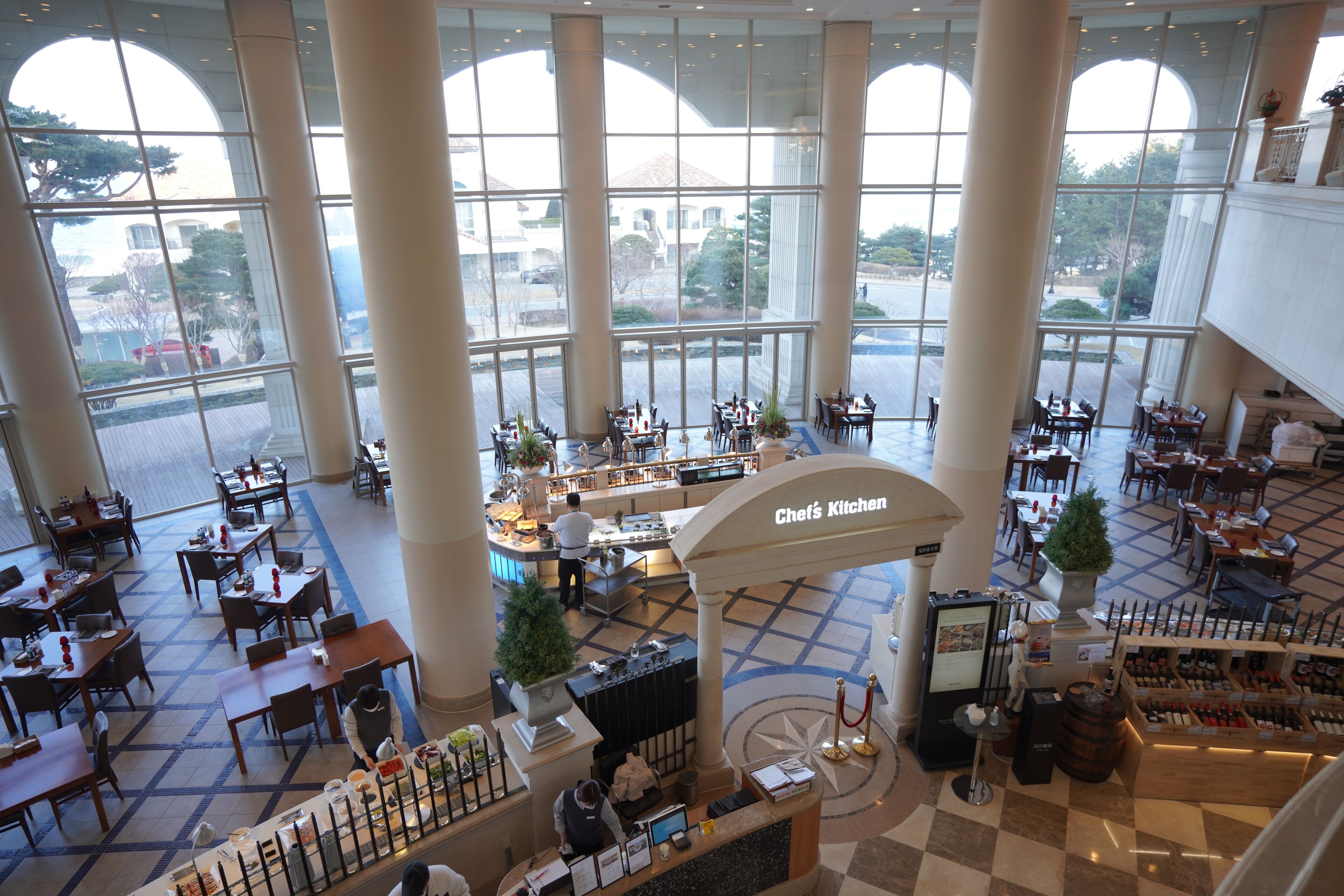 A spacious hotel lobby with multiple dining areas, a central bar, and a wine display.