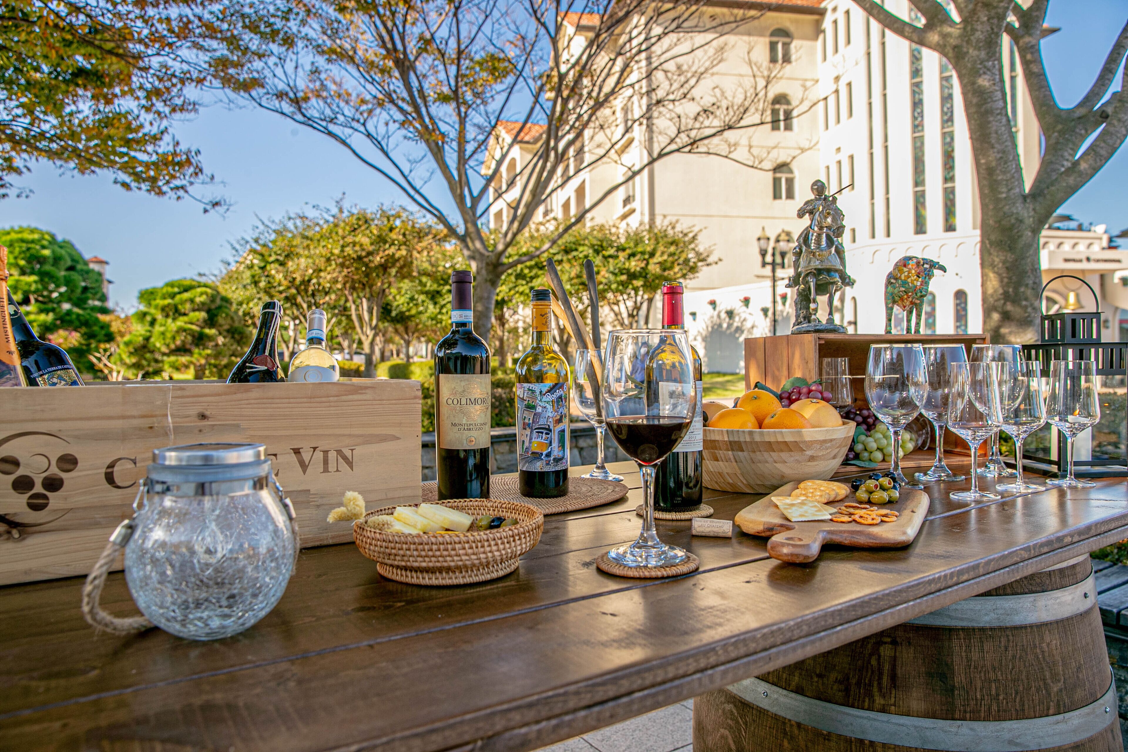Une table en bois, dressée avec des bouteilles de vin, des verres et un saladier rempli de fruits et de collations.