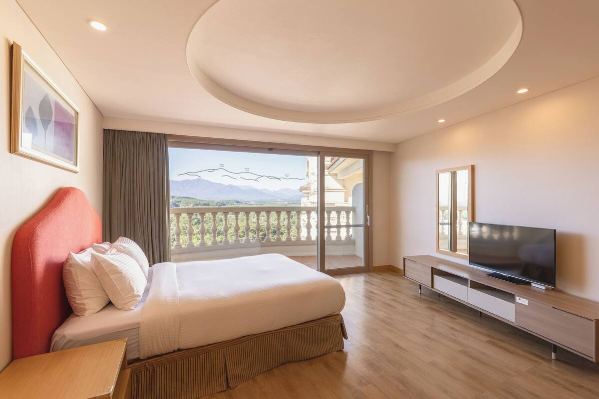 Ett modernt hotellrum med en stor säng, en platt-TV, en balkong med utsikt över bergen och ett trägolv.