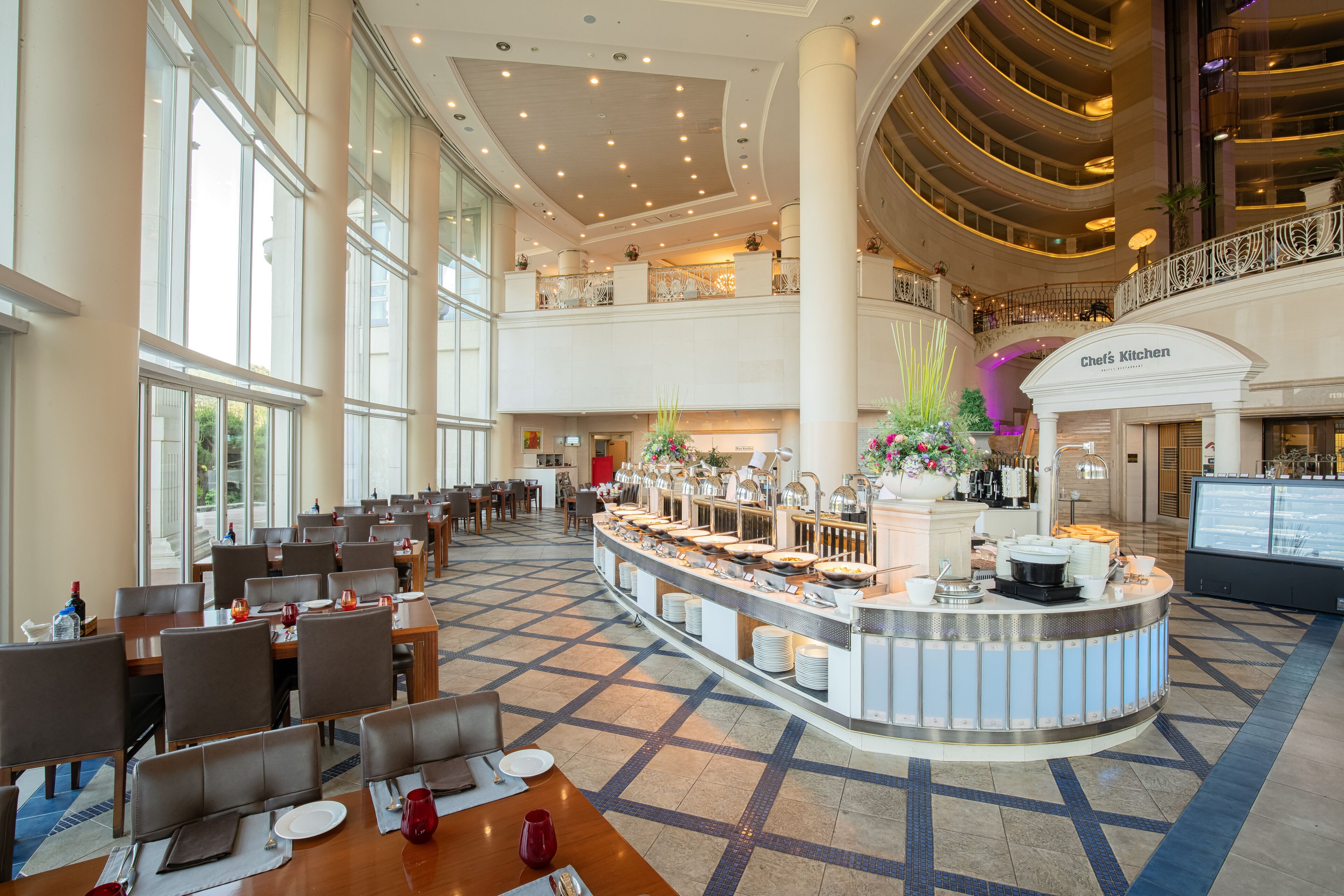 Un hall d’hôtel spacieux avec un buffet central, de nombreuses tables et un atrium à plafond haut.