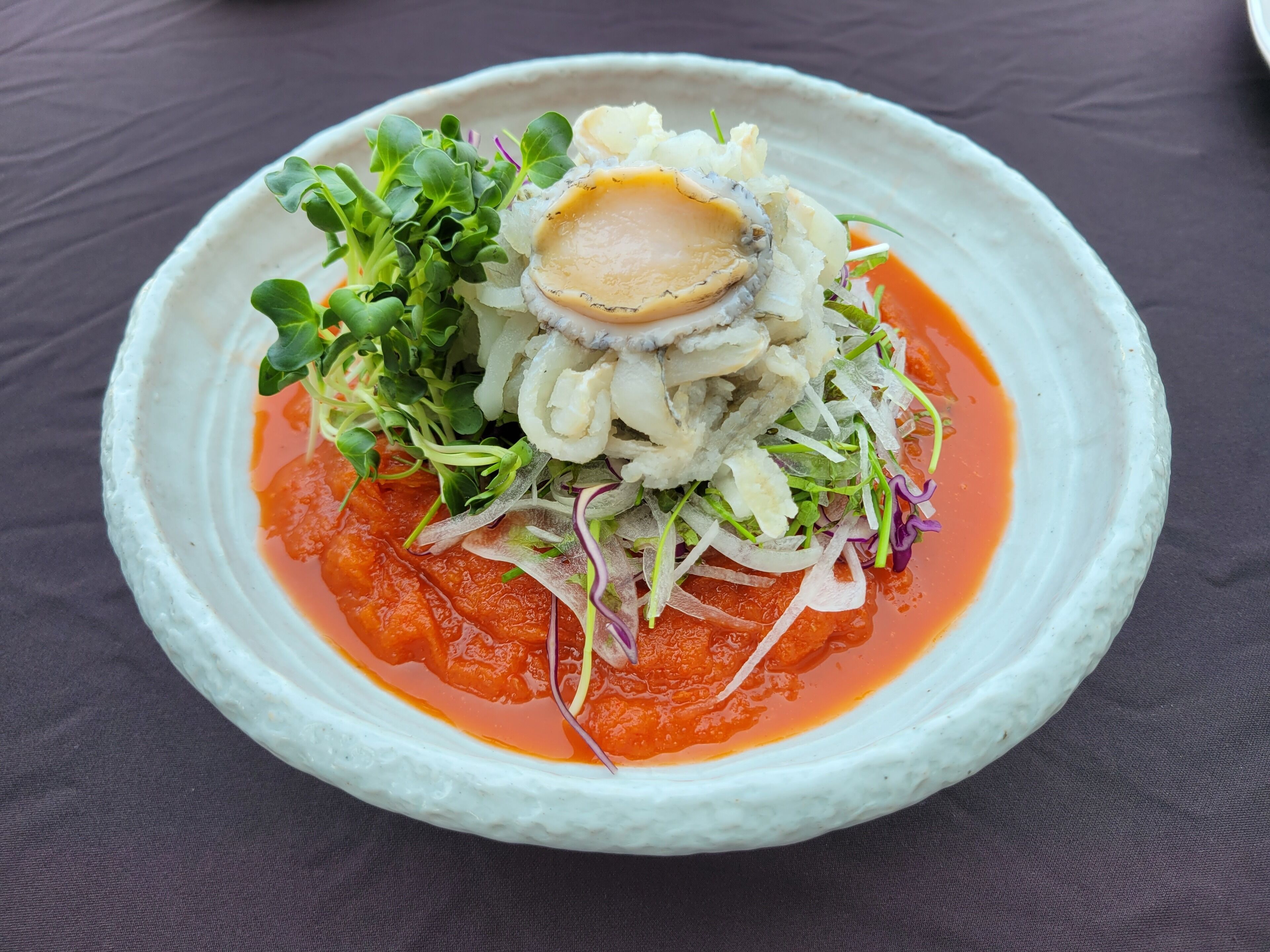 Un plat composé de fruits de mer, de légumes verts et d’une sauce rouge, servi dans une assiette blanche.