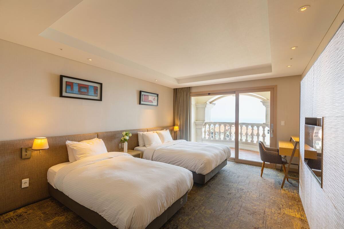 Ett hotellrum med två sängar, ett skrivbord och en balkong.