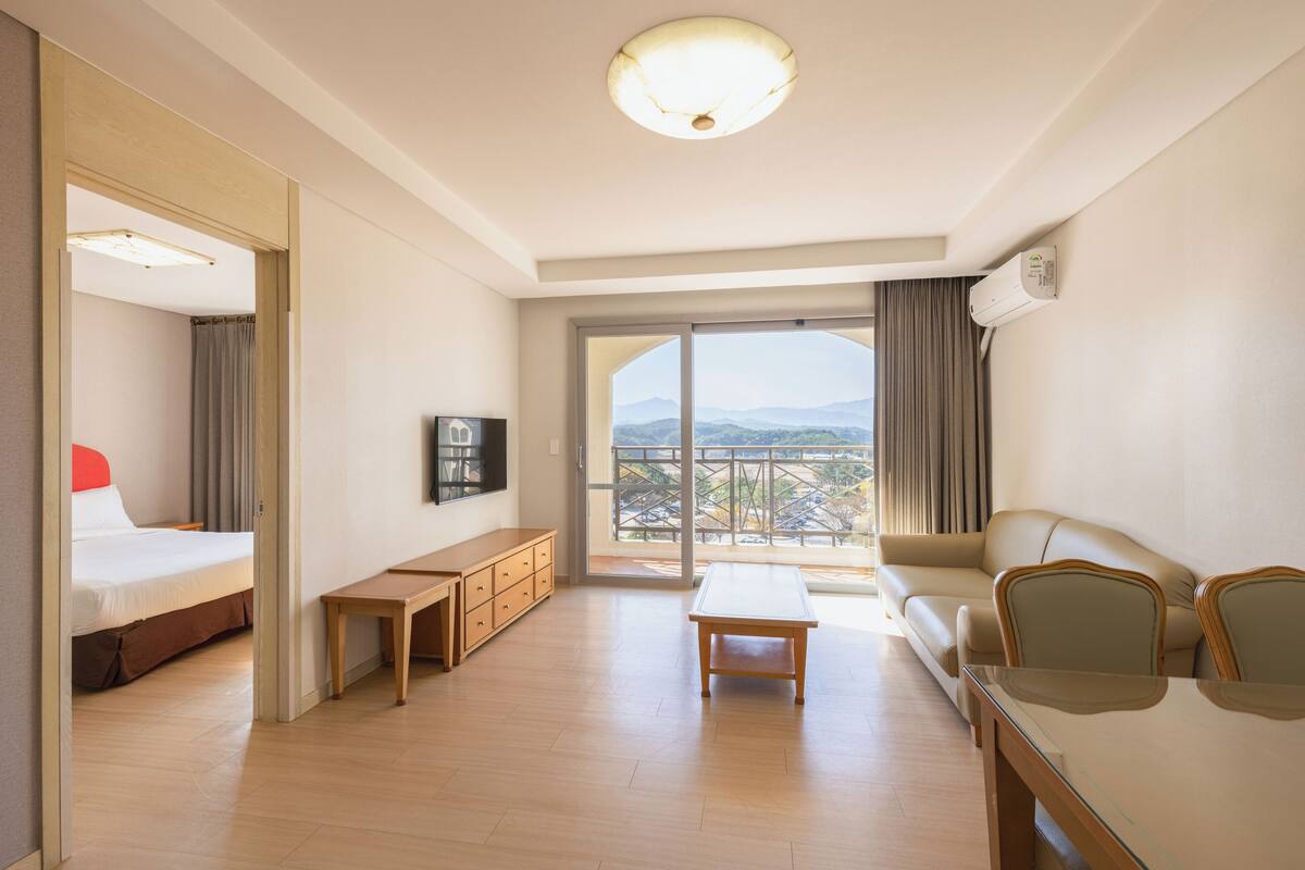 Ett hotellrum med en säng, en soffa, ett matbord, en tv och en balkong med utsikt.