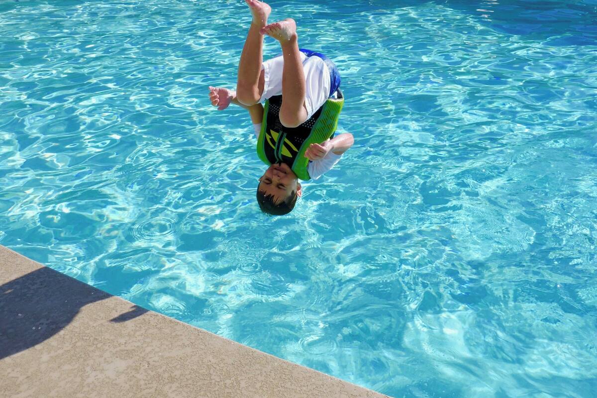 En person dyker ner i en klarblå pool där man tydligt kan se ett djupmärke som visar att djupet är 4 fot.