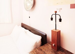 A neatly made bed with white linens, a wooden headboard, and a nightstand with a modern lamp.