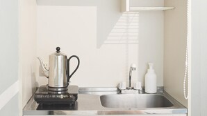 Uma cozinha com cafeteira, pia e prateleira com xícaras e garrafa.