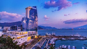 A modern hotel with a glass facade and a prominent 'SONO Caim' sign, located near a marina with boats docked. - Sono Calm Yeosu (Yeosu)