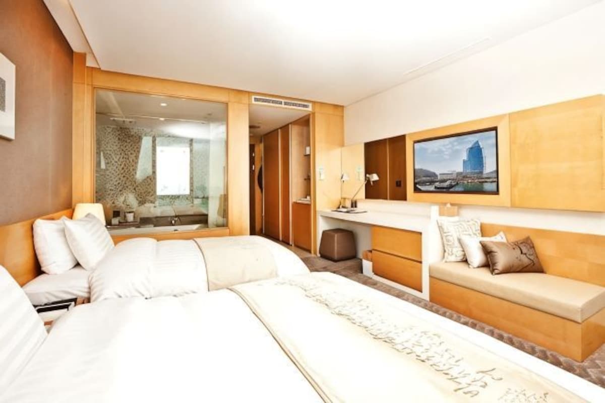 Ett hotellrum med en stor säng, en soffa, en tv och ett badrum som syns genom en glasdörr.