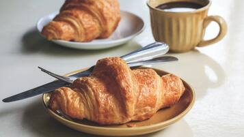 Un croissant sobre un plato con un cuchillo, una taza de café, y otro croissant sobre un plato al fondo.