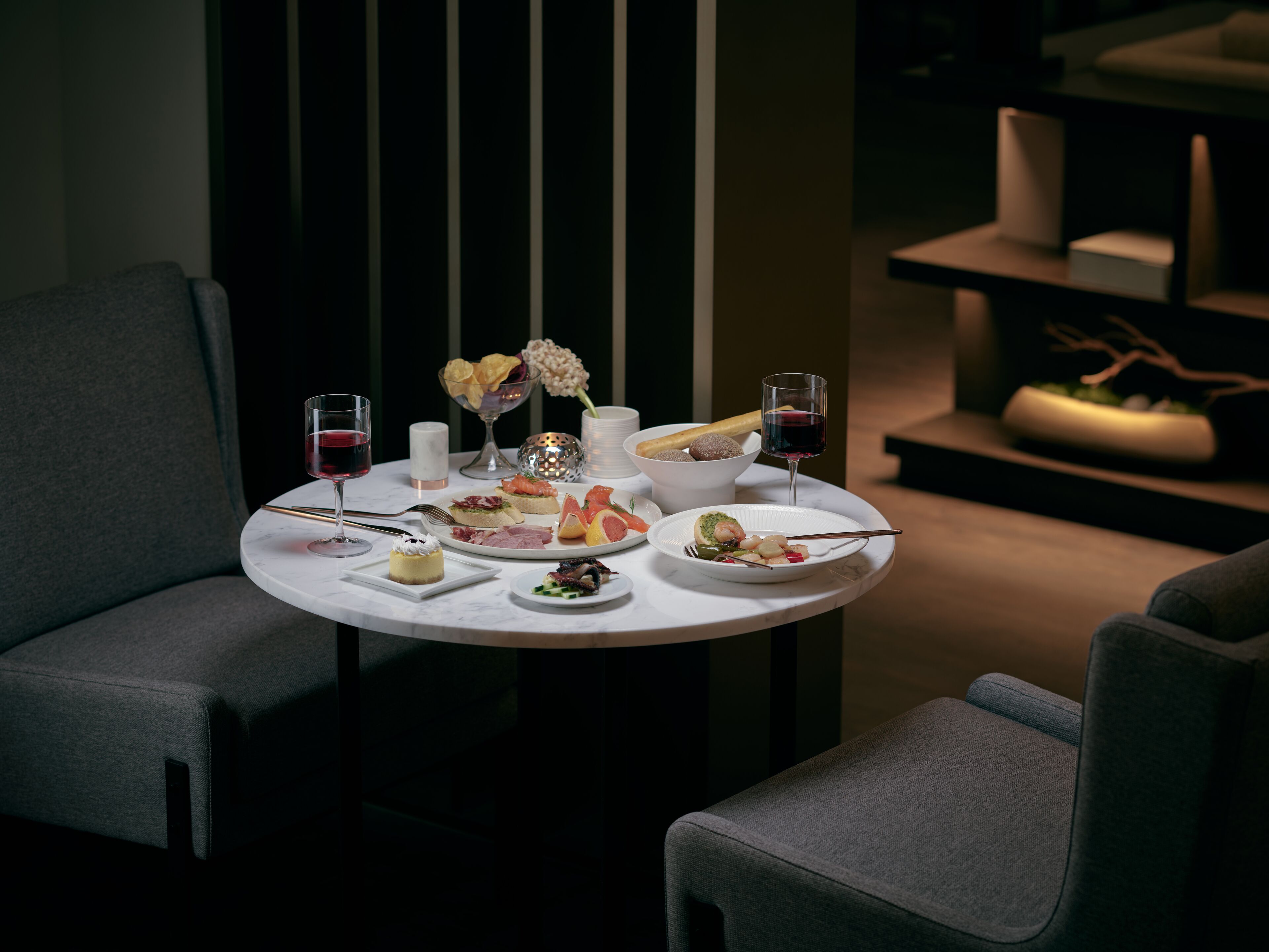 A dining table set with various dishes, glasses of red wine, and a vase with flowers.