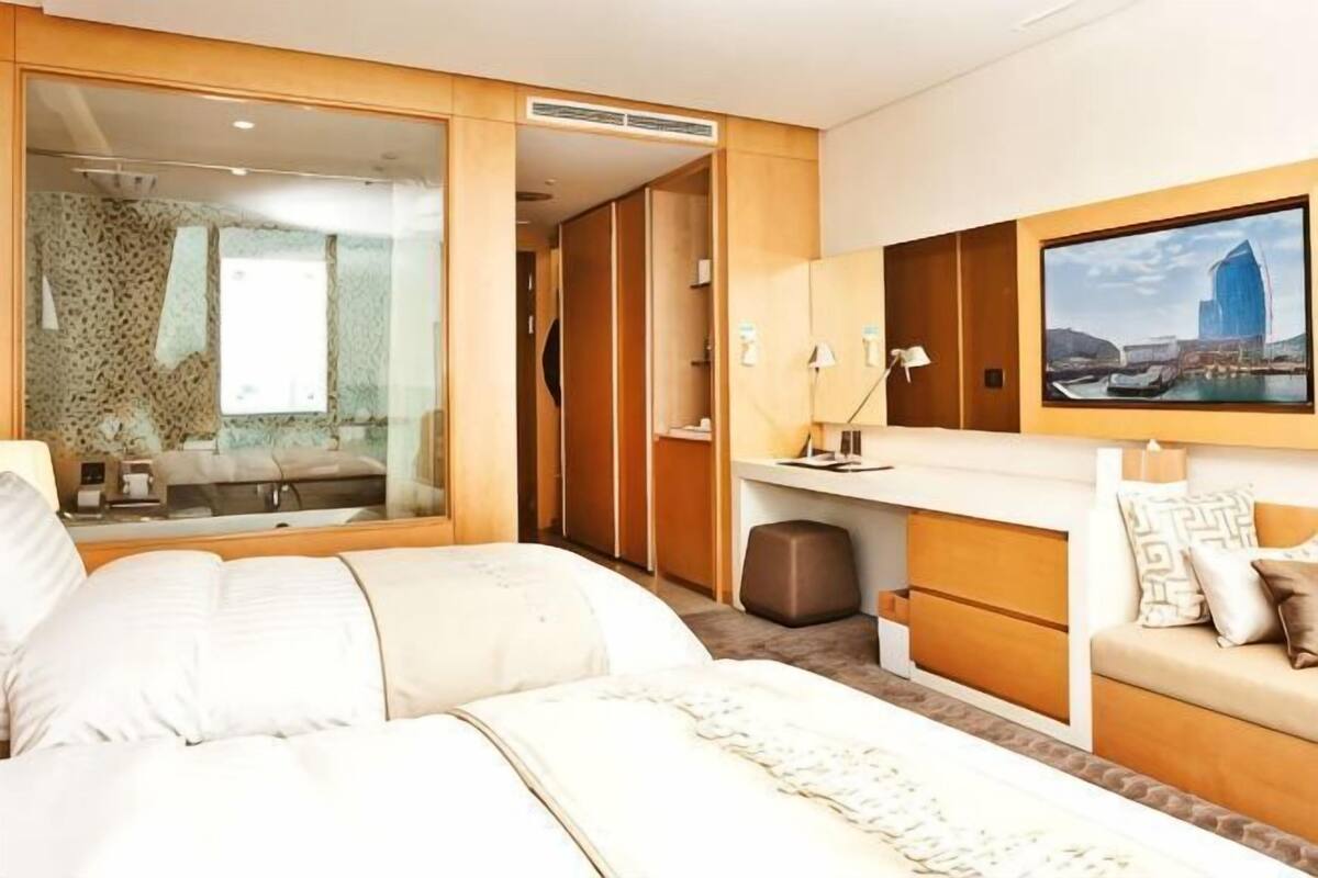A hotel room with a bed, a desk, a mirror, a wardrobe, and a painting on the wall.