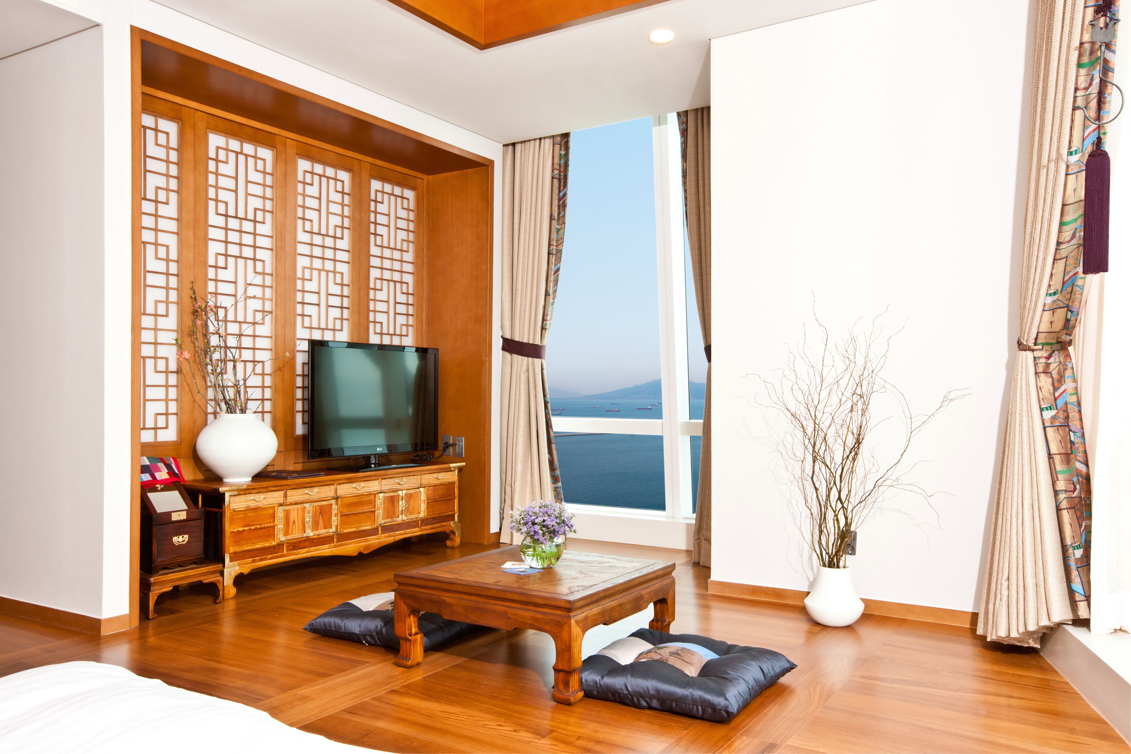 Un salón moderno con un mueble bajo para el televisor de madera, un televisor de pantalla plana, una mesa de centro y un ventanal con vistas al mar.