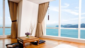 A bedroom with a large window, wooden floor, a bed, a small table with a vase, and a hanging decoration. - Sono Calm Yeosu (Yeosu)