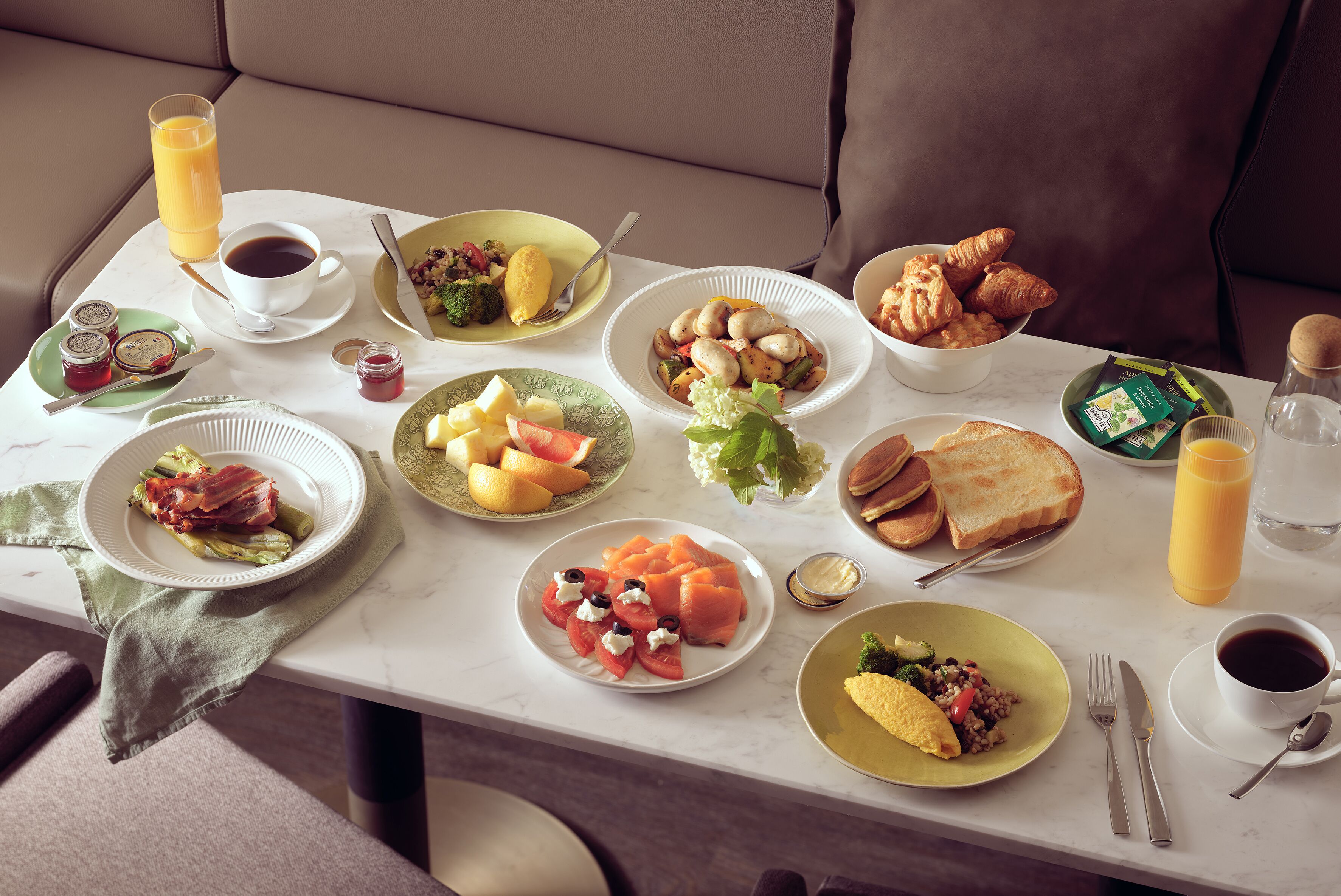 Una mesa de desayuno con diferentes platos, como tostadas, croissants y fruta.