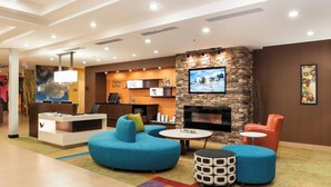 A lobby with a reception desk, seating area with sofas and ottomans, a fireplace, and a television screen.