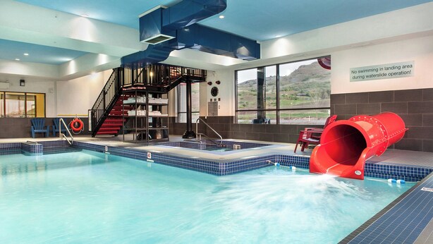 An indoor swimming pool with a red slide, a staircase, and a warning sign about no swimming in the landing area during operations.