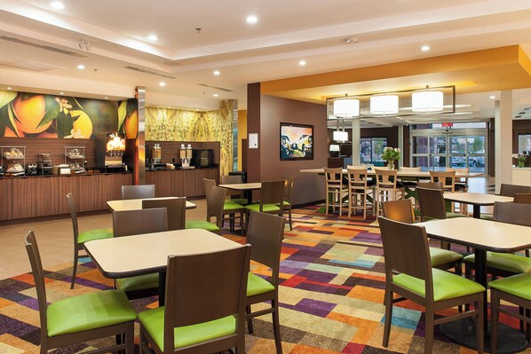 A hotel lobby with multiple dining tables and chairs, a coffee station, and a large mural on the wall.