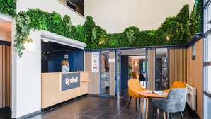 A reception area with a wooden desk, a reception desk, and a seating area with chairs. - Kyriad Dieppe - Saint Aubin Sur Scie (Saint-Aubin-sur-Scie)