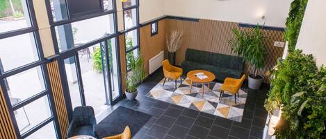A modern interior with large windows, a green sofa, yellow chairs, and a geometric patterned rug.
