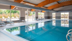 An indoor swimming pool with clear blue water, wooden beams, and sunlit windows. - Kyriad Dieppe - Saint Aubin Sur Scie (Saint-Aubin-sur-Scie)