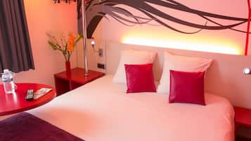 Hotelkamer met een groot bed, rode kussens, een rode nachtkastje, een rode tafel met een waterfles en een afstandsbediening, en een wand met een rood bloemenmotief.