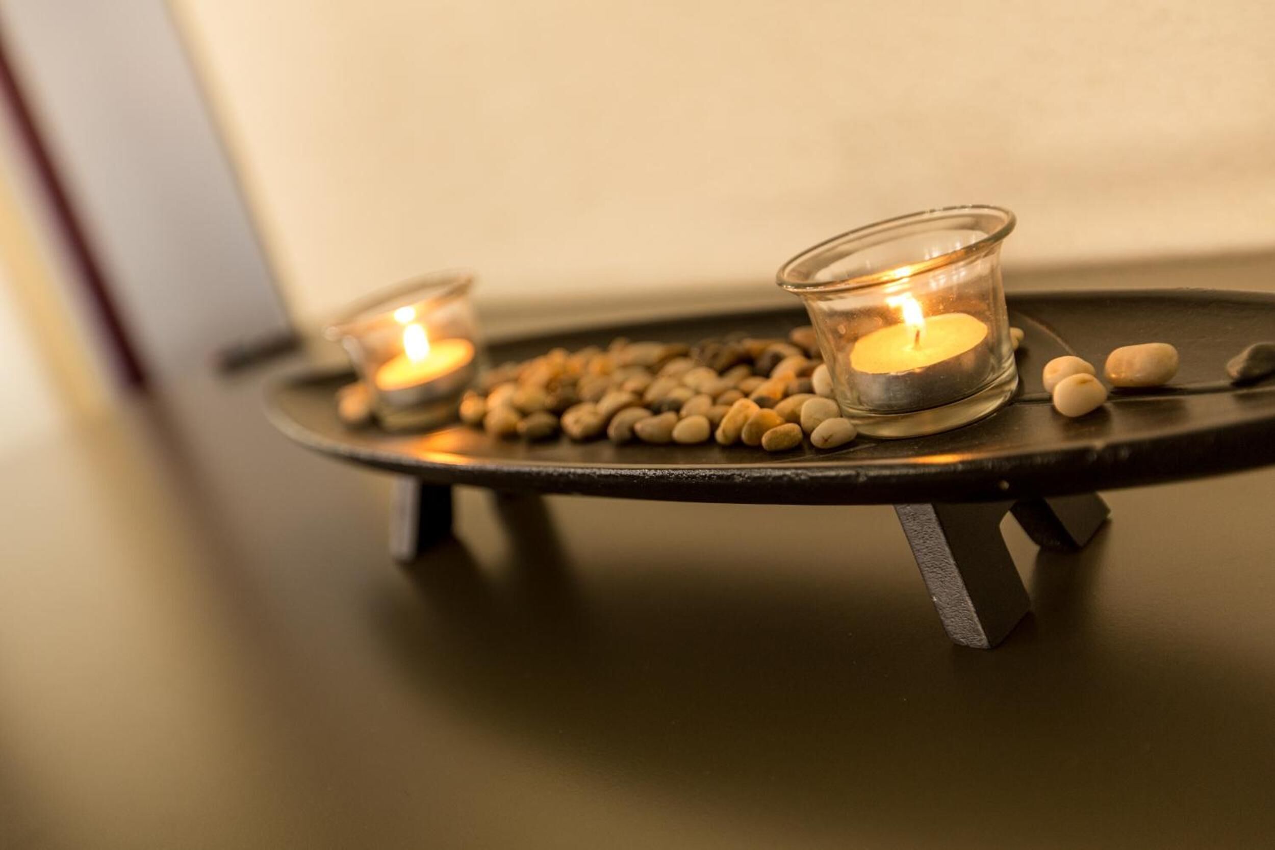 Un candelabro con dos velas encendidas y guijarros dispersos sobre una mesa.