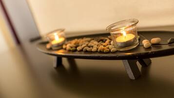 A candle holder with two lit candles and scattered pebbles on a table.