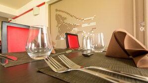A neatly set dining table with clear glassware, cutlery, and a brown napkin folded on the placemat. - Hôtel Inn Design & Restaurant Sedan (Sedan)