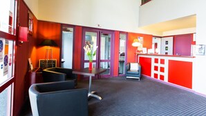 A hotel lobby with a reception desk, seating area, and a staircase. - Hôtel Inn Design & Restaurant Sedan (Sedan)