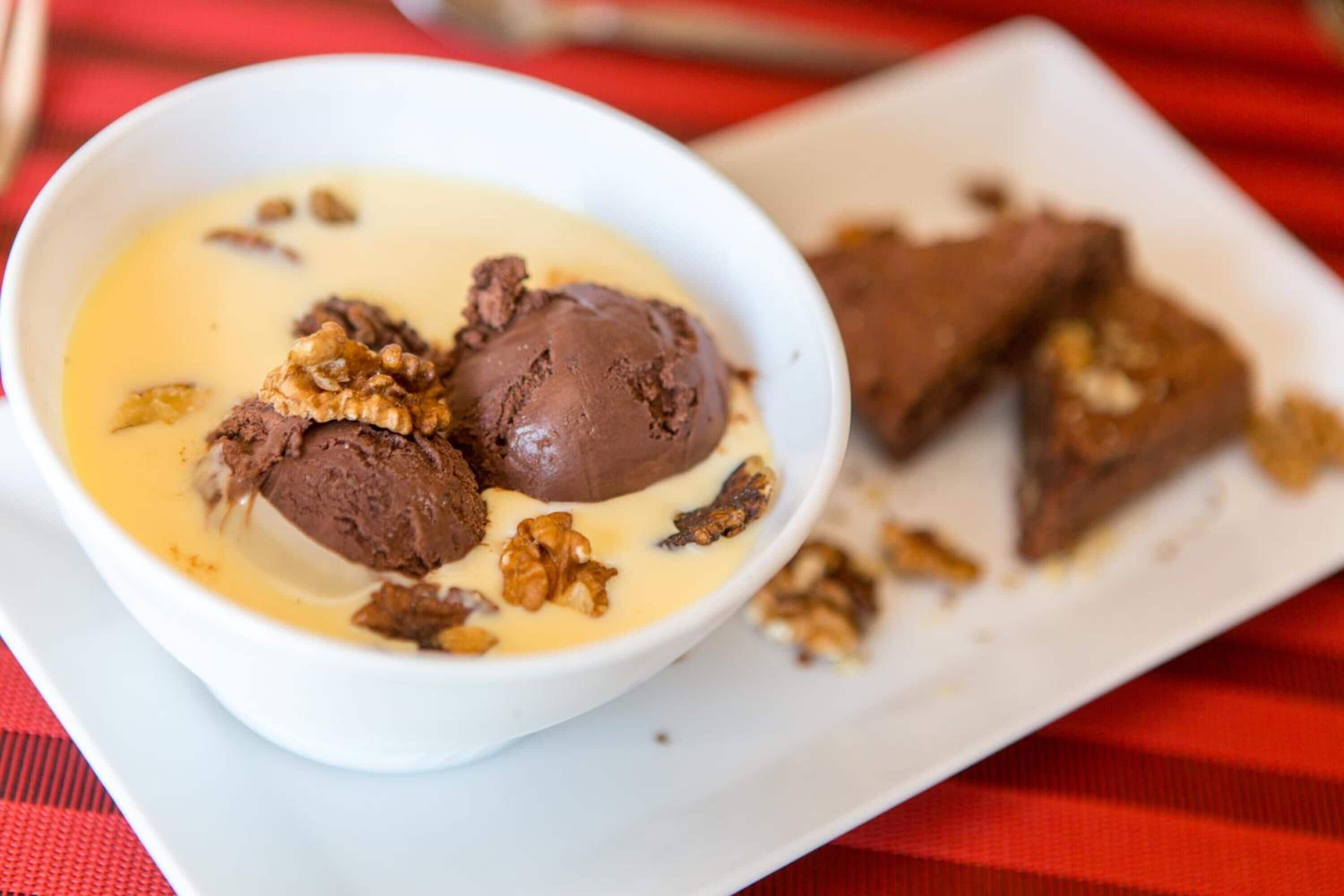 A bowl of chocolate ice cream with nuts on a white plate.