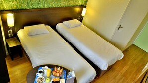 A hotel room with two single beds, a small table with breakfast items, and a wall with a grass-like texture. - Hôtel Inn Design & Restaurant Sedan (Sedan)