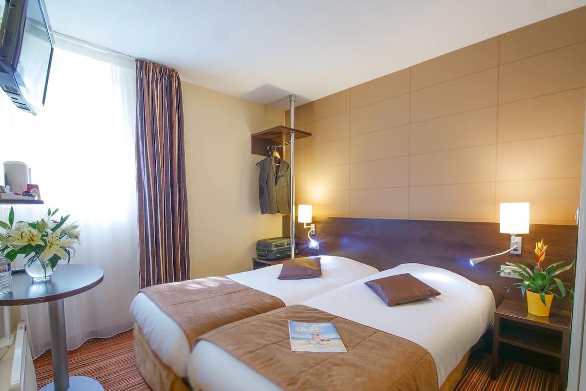A hotel room with two beds, a desk, a lamp, a potted plant, and a window with curtains.