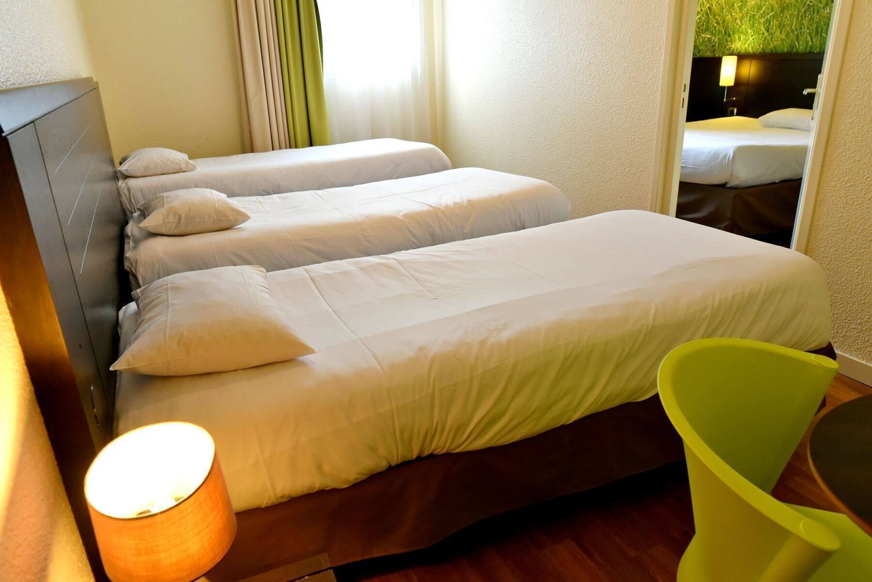 A hotel room with two beds, a wooden headboard, a green chair, and a lamp.
