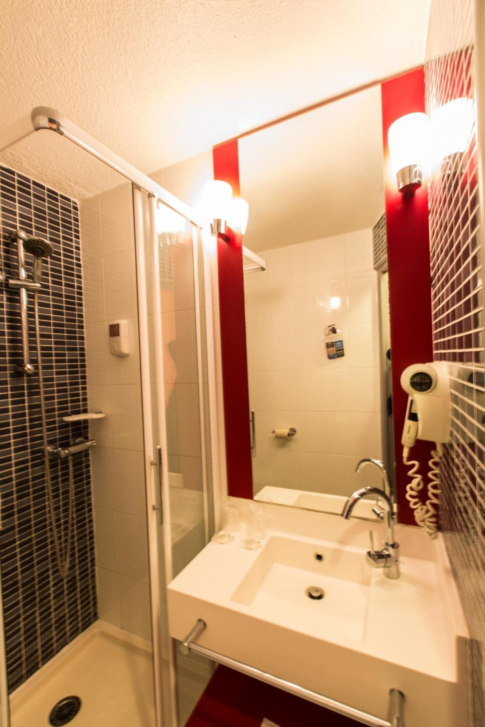 A bathroom with a glass-enclosed shower, a white sink, and a mirror with red accents.