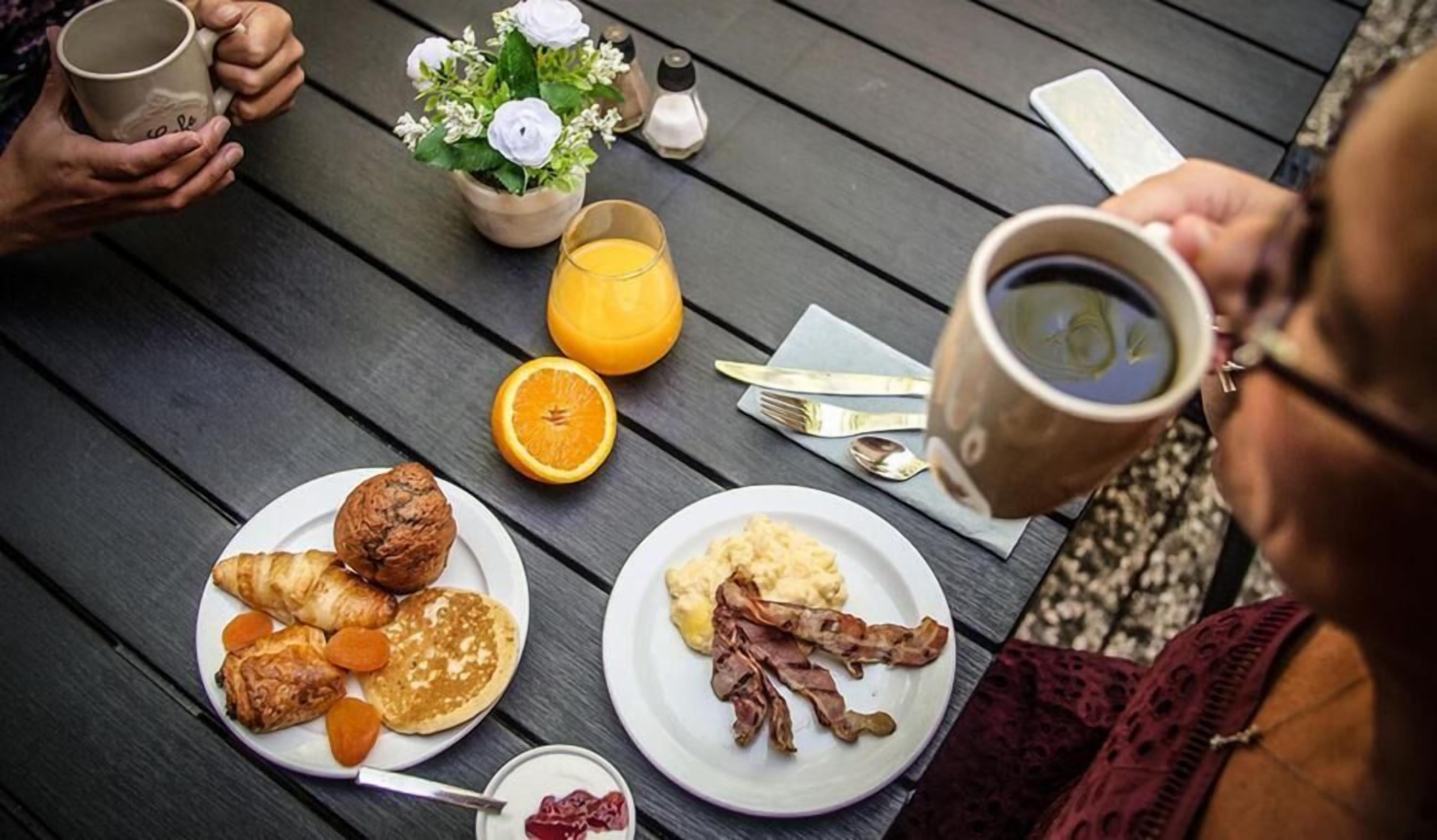 A breakfast setting with plates of food, a coffee cup, and a flower vase on a wooden table.