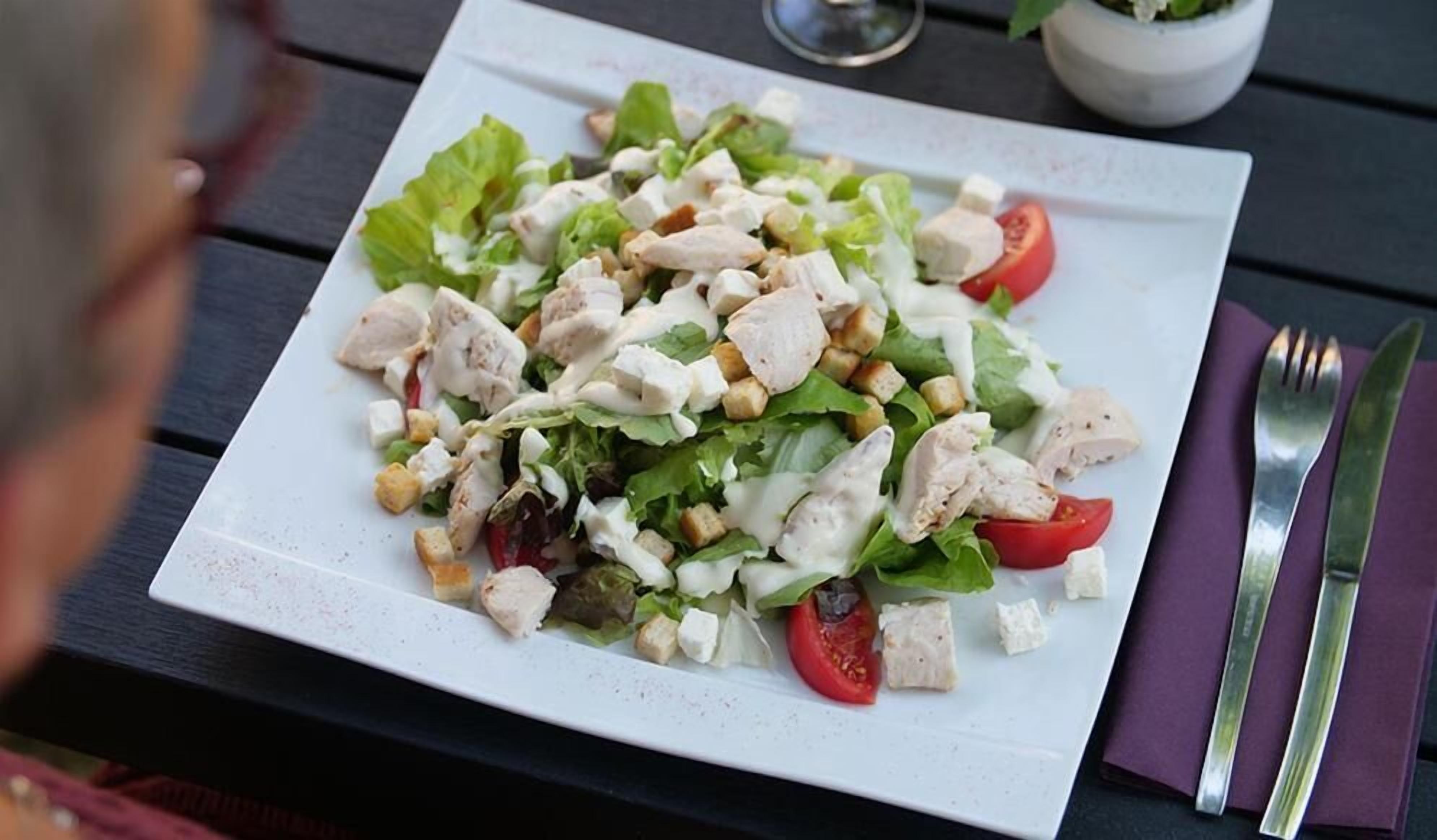 Een bord salade met sla, tomaten en croutons op een wit bord.