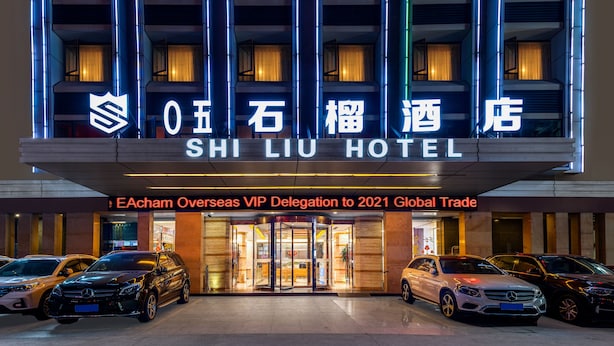 Exterior do Hotel Shi Li com fachada moderna, várias varandas e uma placa indicando ser a Delegação VIP do ECham Overseas para o Comércio Global de 2021.