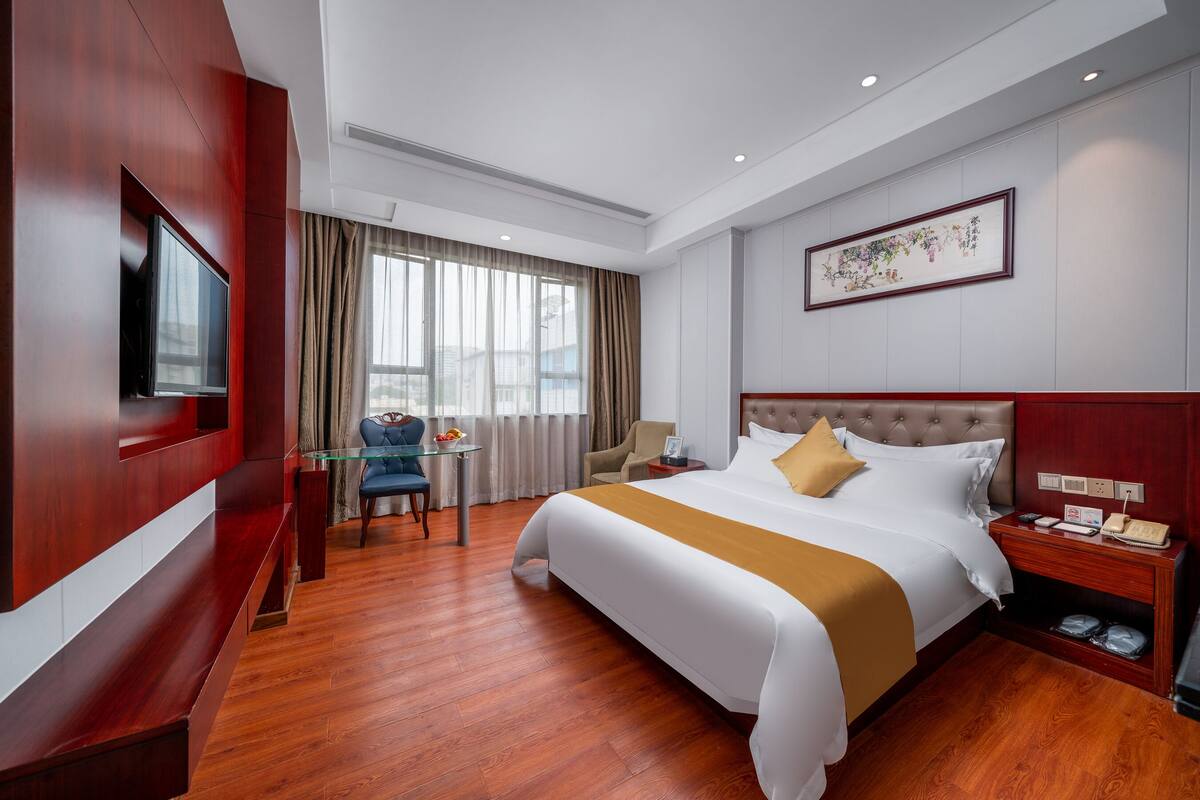 Een hotelkamer met een groot bed, een televisie, een bureau met stoel, en een raam met gordijnen.